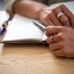 Handen met een pen naast een opengeslagen notitieboek